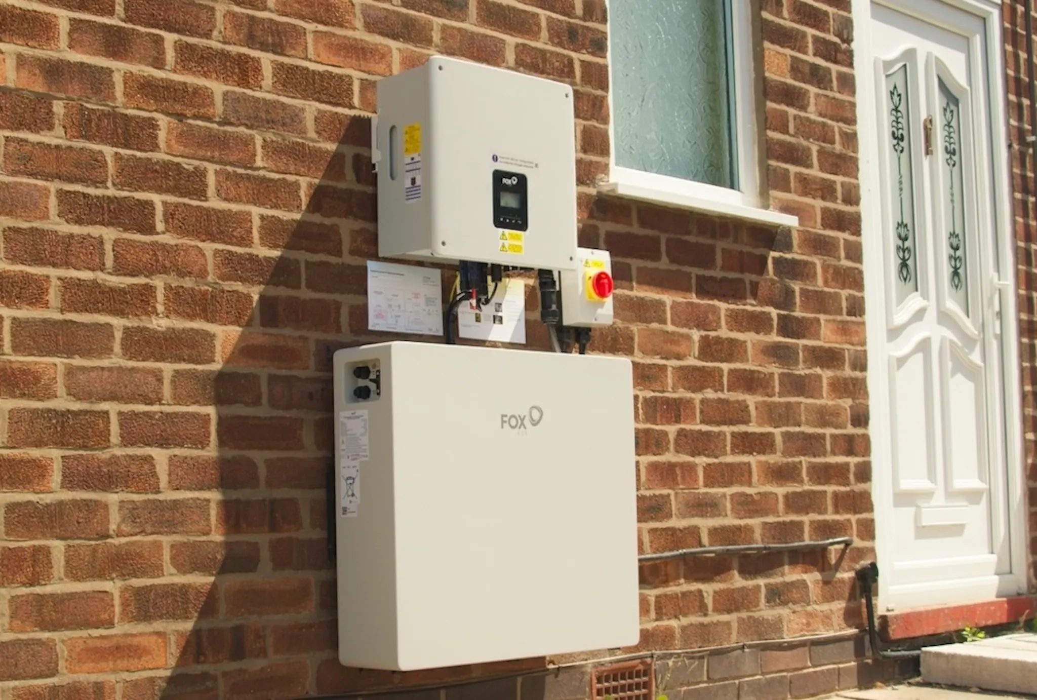 a white battery and inverter on a brick wall, near a white door