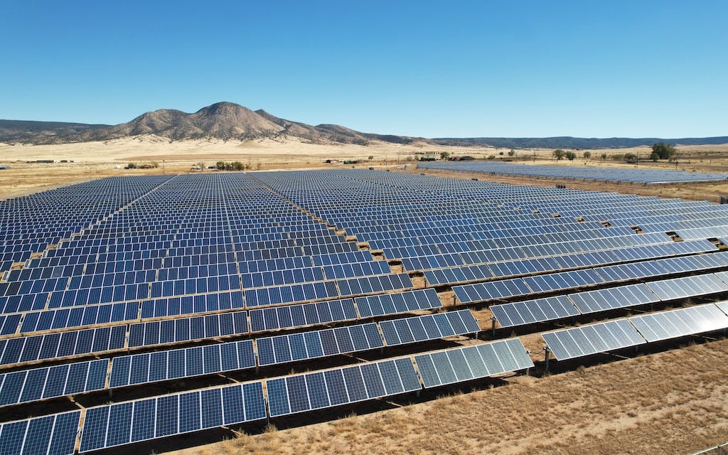 A huge solar farm in the desert, a rocky mountain in the background, blue sky