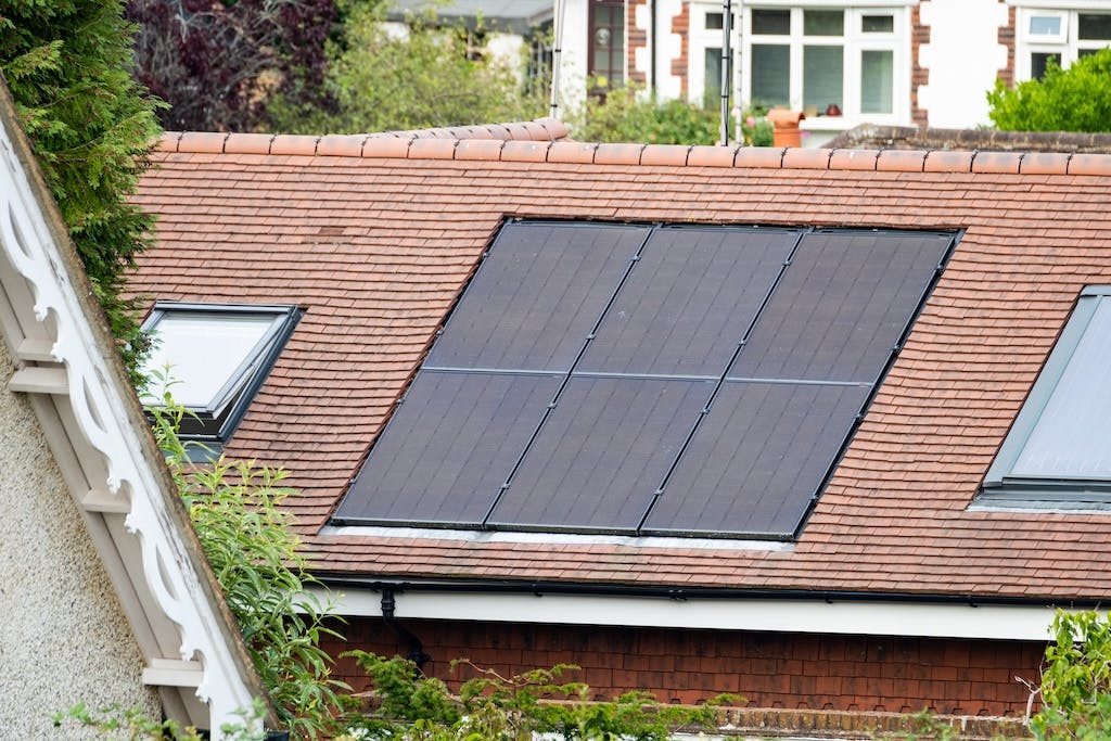 Six black monocrystalline solar panels on a brown rooftop in the UK, velux windows either side