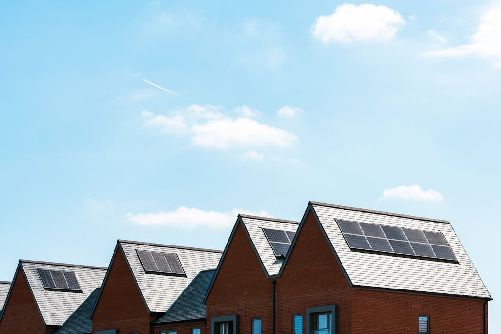 solar panels on grey roofs of brick houses under a blue sky with wispy clouds
