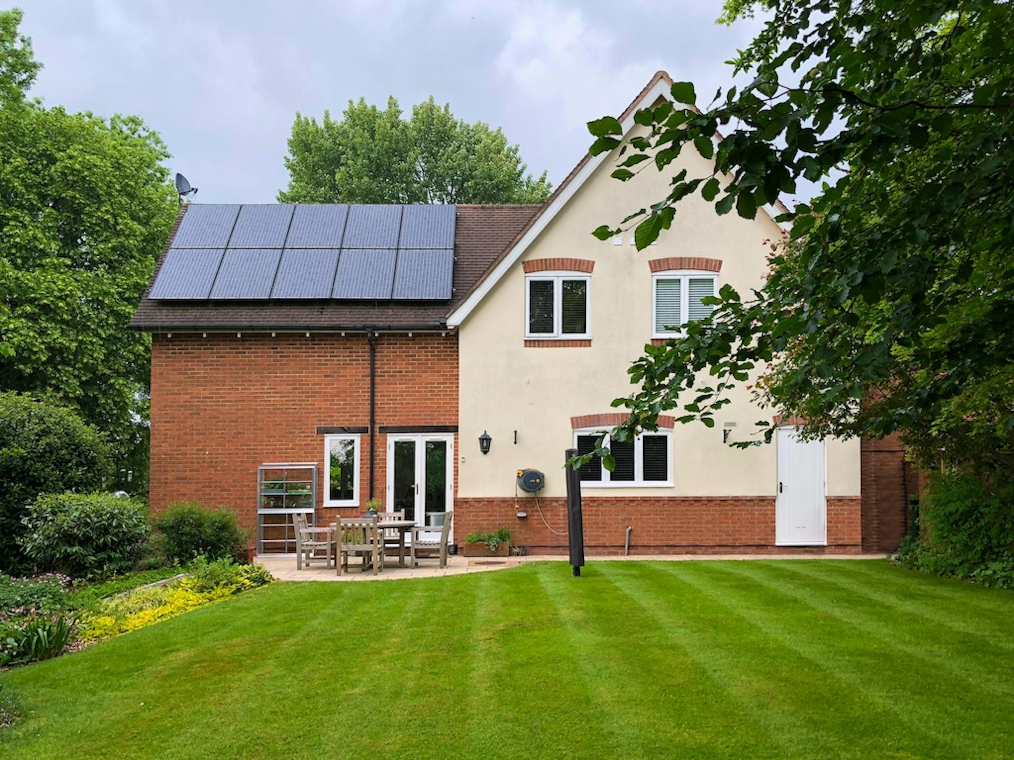 solar panels on a brown roof, on a brick house, in front of a green garden