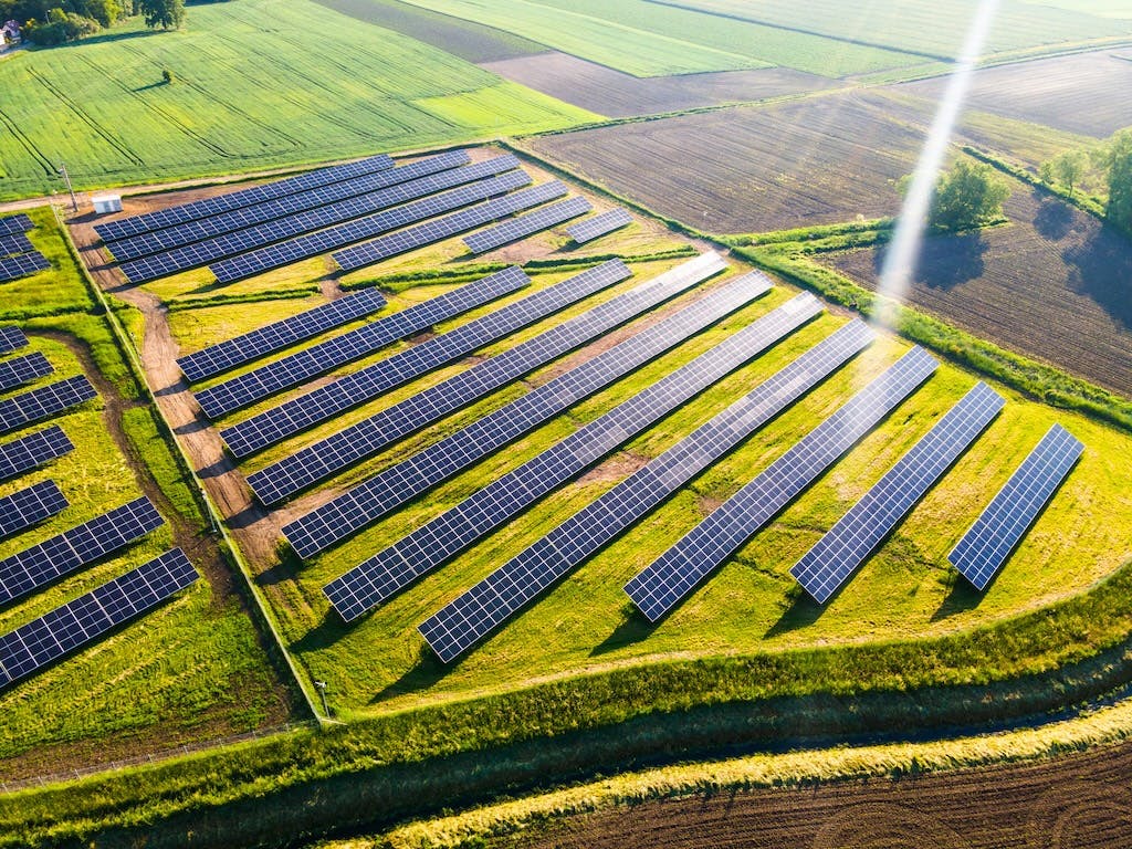 Aerial shot of a solar farm in green fields, sunny weather, more countryside in the distance
