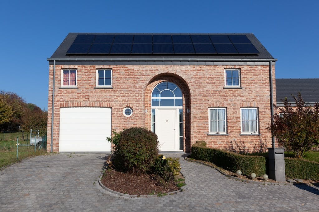 A black monocrystalline solar panel array on a large house in the UK, grey driveway and blue sky in the background