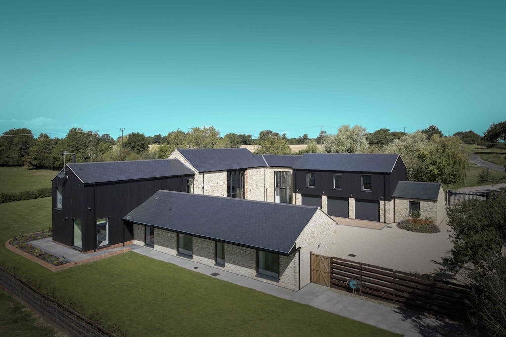 A detached house with solar tiles on every roof, surrounded by gardens and trees, under a blue sky