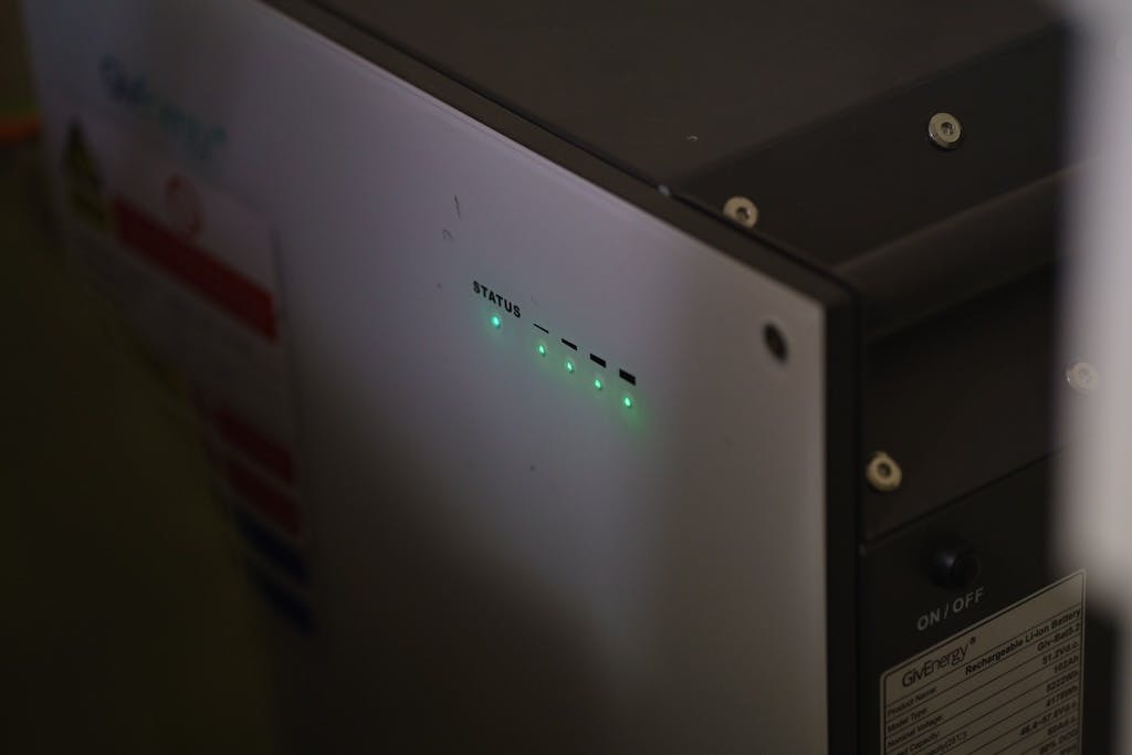 A shadowy close-up shot of a GivEnergy storage battery in a garage, with glowing green lights showing that it's working