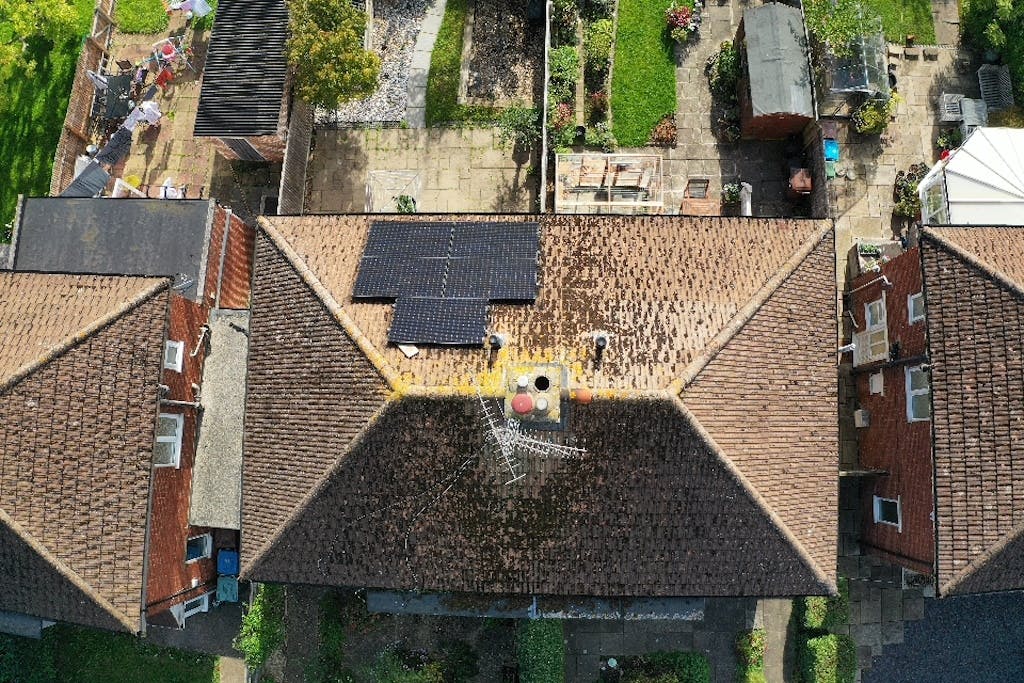 A terracotta roof seen from above, with black solar panels on the front, next to other roofs and gardens