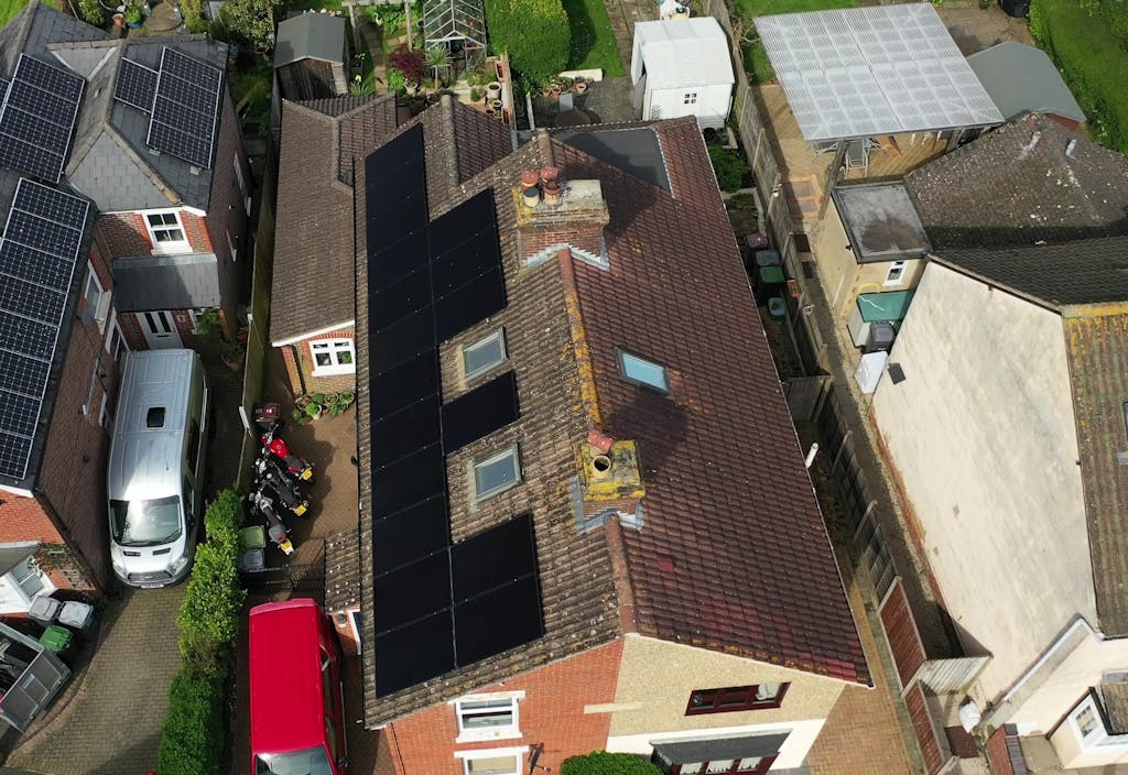 black solar panels on a brown roof, surrounded by trees, cars, gardens, and other houses