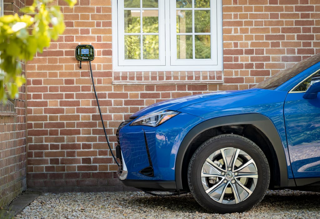 A blue electric car getting charged by an Ohme home charging point, against a brick wall (photo credit: Ohme)