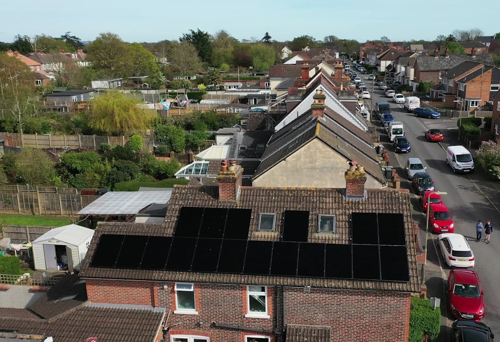 black solar panels on a brown roof, surrounded by trees, cars, gardens, and other houses