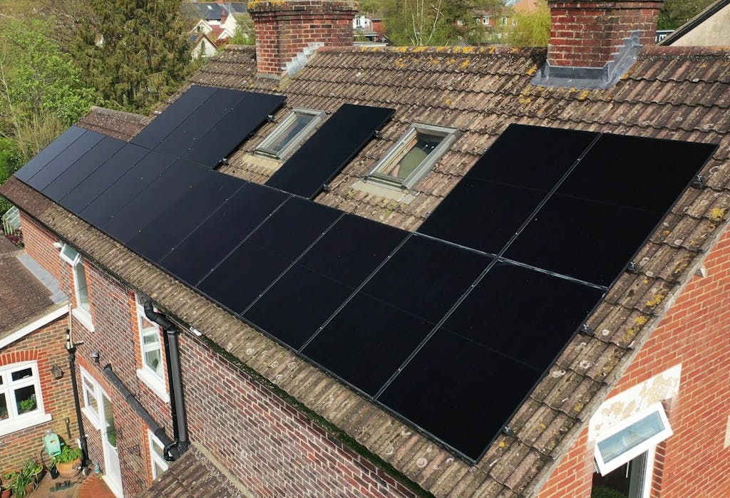 black solar panels on a brown roof, surrounded by trees, cars, and other houses