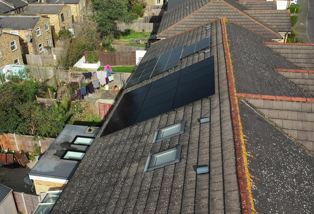 black solar panels on a brown roof, surrounded by trees and other houses