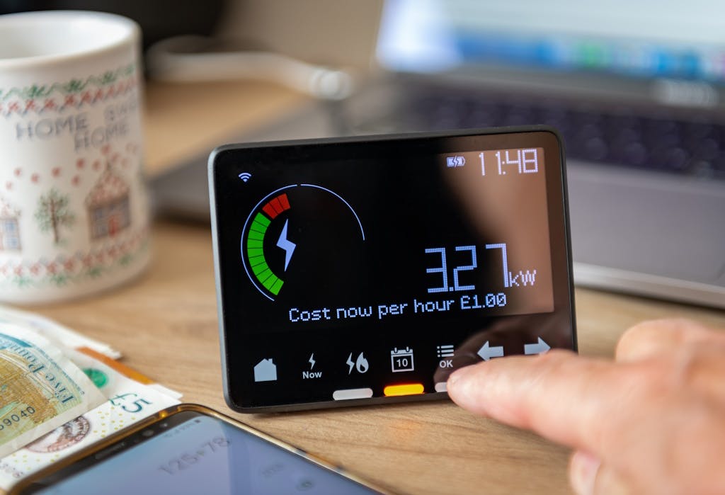 a smart meter on a table, next to some money, with a finger pointing towards the smart meter