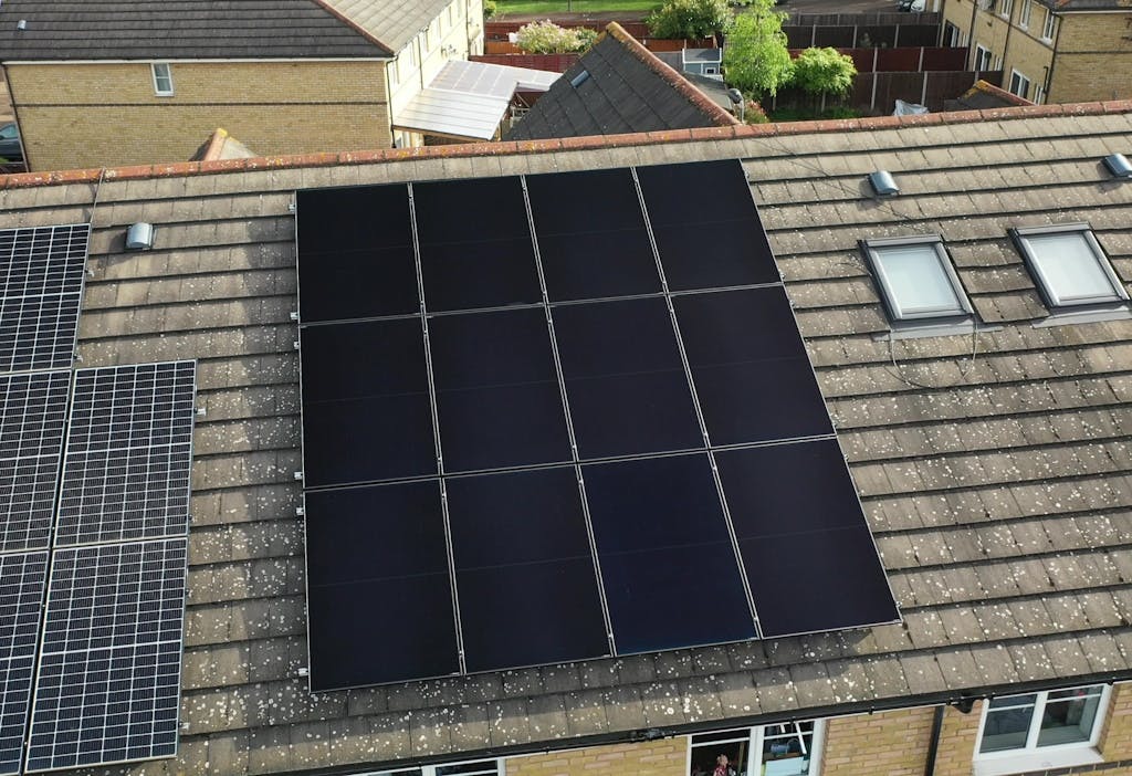 black solar panels on a brown roof, next to blue solar panels on a different home's roof