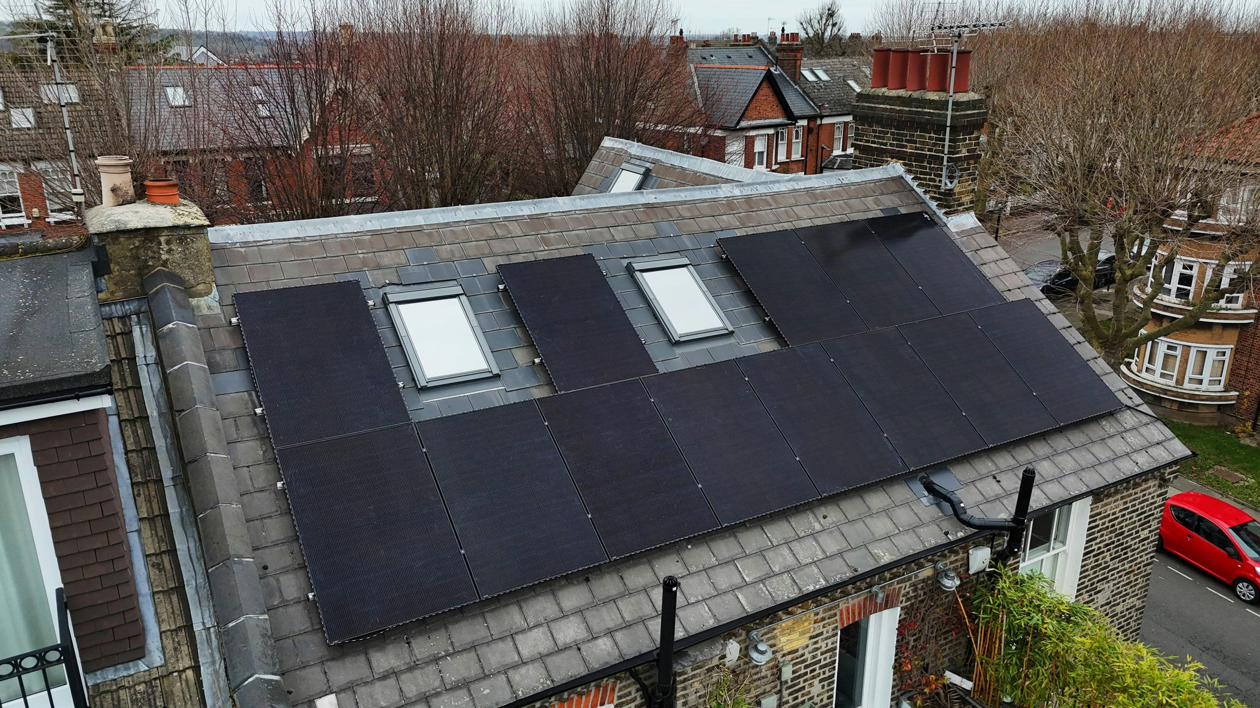 Black solar panel array on a rooftop in north London, red car driving past