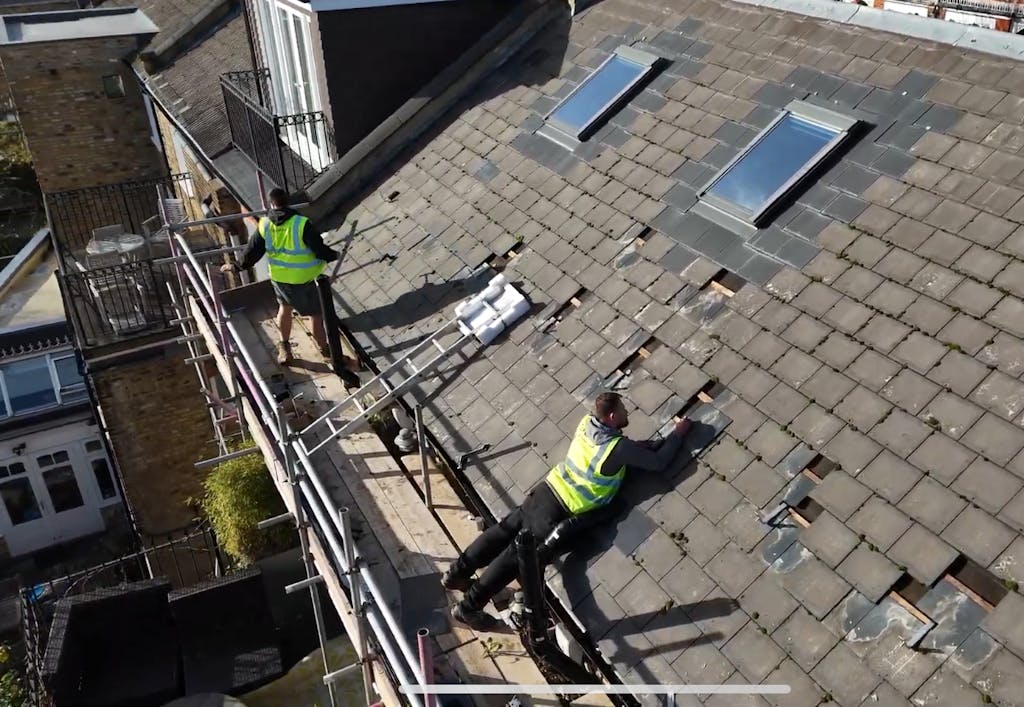 two installers in high-vis vests on a brown roof in the middle of a solar panel installation