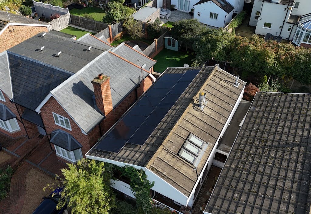 Black solar panels on a brown roof, next to other houses