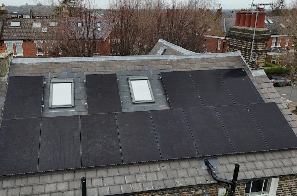 Black solar panels on a grey slate roof, around two skylights