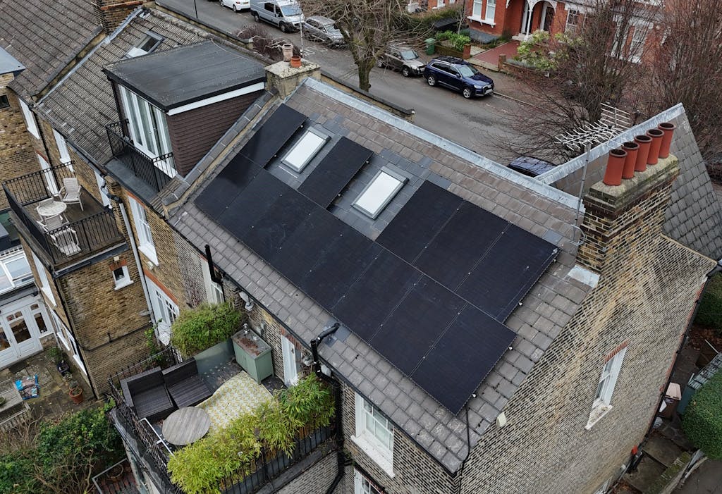 Black solar panels on a grey slate roof, next to another house with a dormer