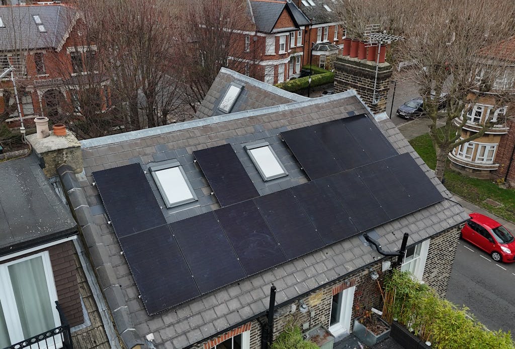 Black solar panels on a grey slate roof, next to another house