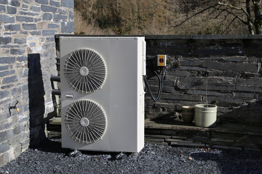 a white heat pump by two grey stone walls, on grey gravel