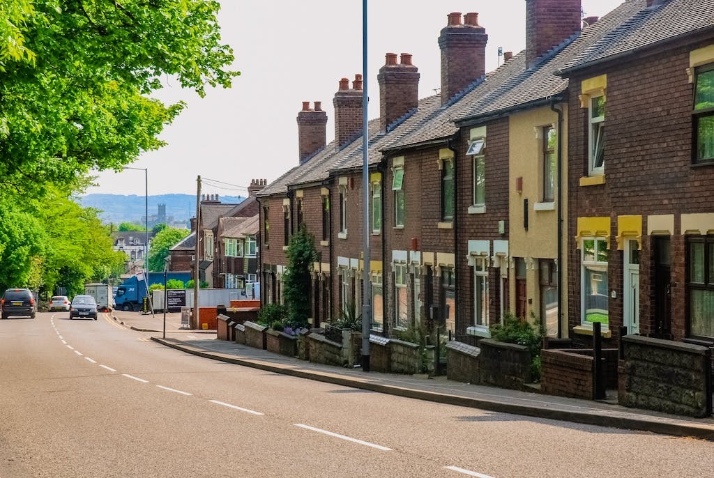 Row of terraced houses along a road in the North East, cars passing by, trees to the left