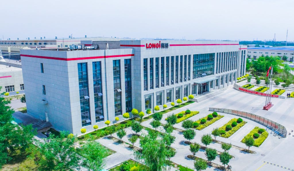 A white factory with LONGi written on the outside, in front of trees