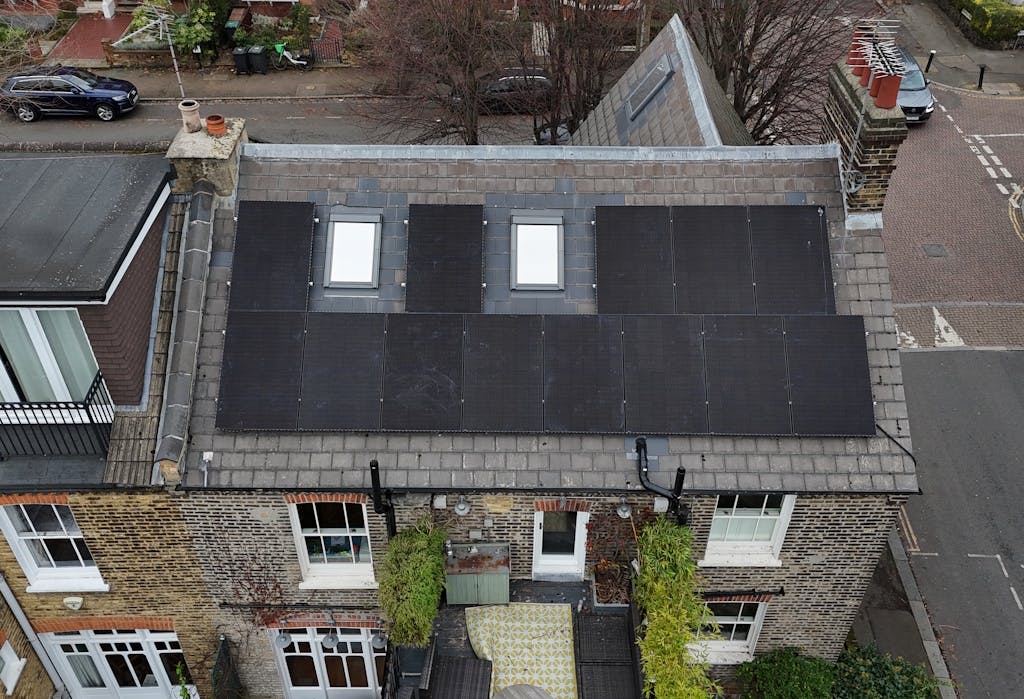 Black solar panels on a grey slate roof, around two skylights