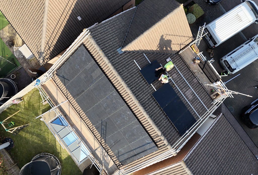 a brown roof with black solar panels, and two installers in hi-vis jackets installing more panels