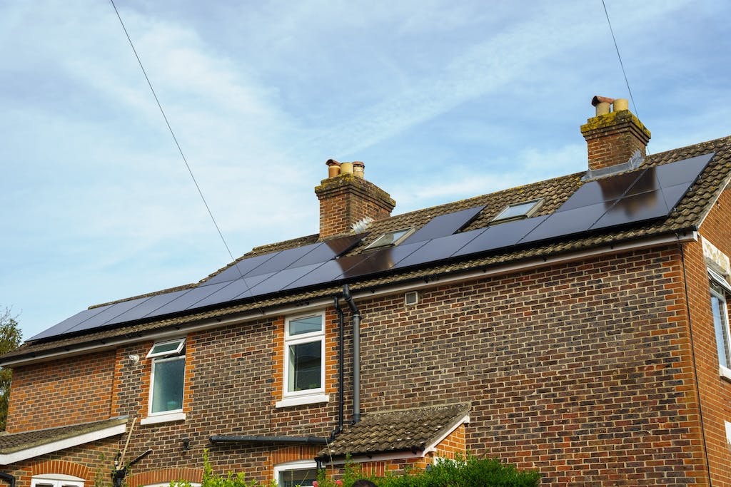 A black monocrystalline solar panel array on a UK rooftop, blue skies in the background