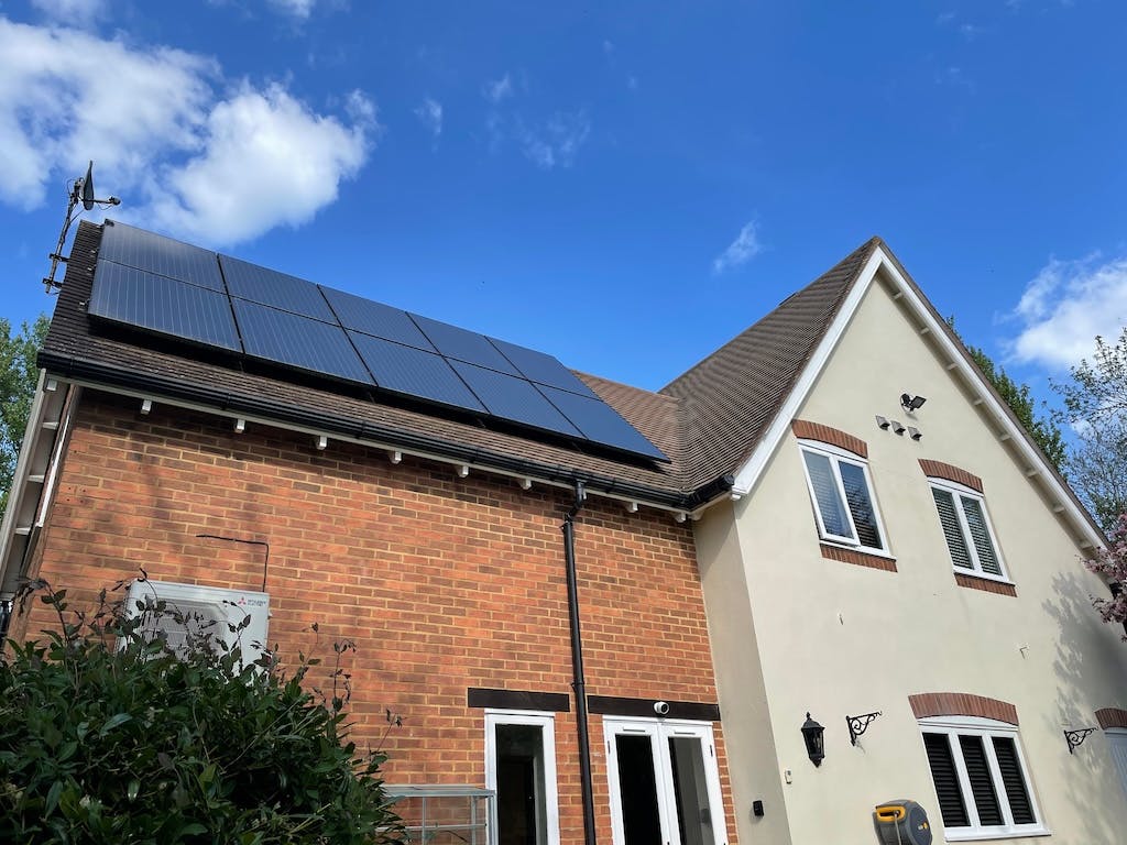 Ten black solar panels on a UK rooftop, photo taken from below, blue sky in background