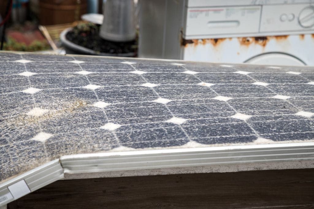 A solar panel in severe disrepair, bent on one side, with cracked glass and dirt