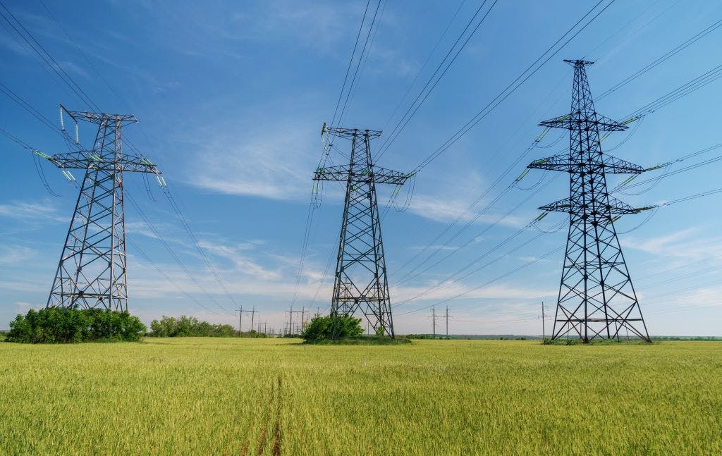 Three electricity pylons in a green field with blue sky behind them