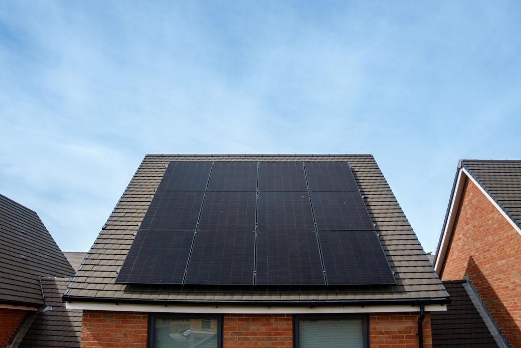 Photo of a brick house with black solar panels on a grey roof, under a light blue sky