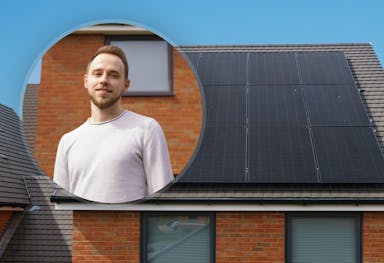 Circle including a smiling man in a white jumper, against a background of a house with black solar panels on its roof, blue sky in background