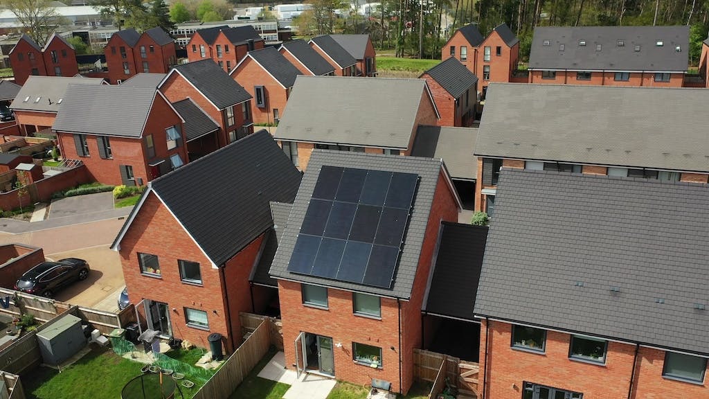 A collection of houses in Hampshire, one with twelve black solar panels on its roof, trees in the background