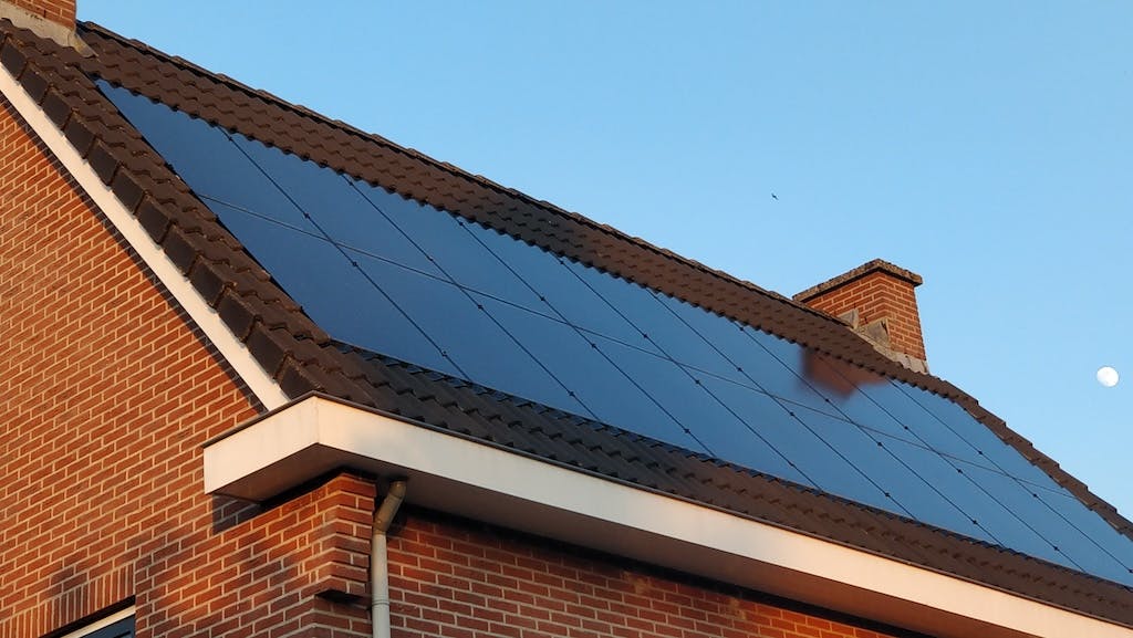 An array of black, roof-integrated solar panels on a UK residential rooftop, blue sky in background