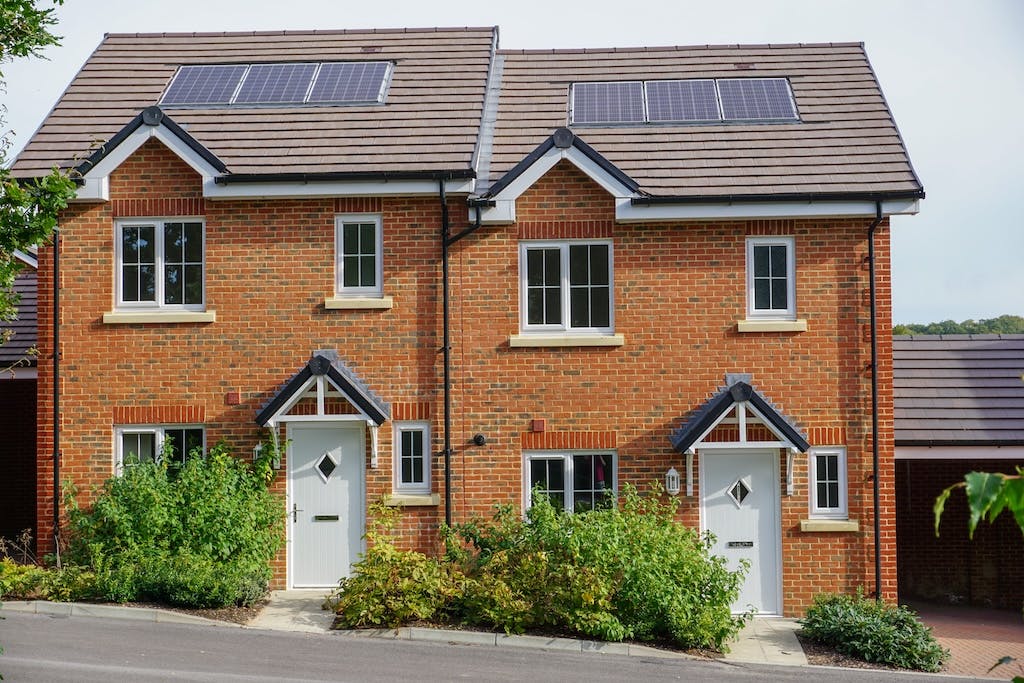 Two semi-detached new build homes in the UK, each with three solar panels on their roofs, hedges at the front of each home