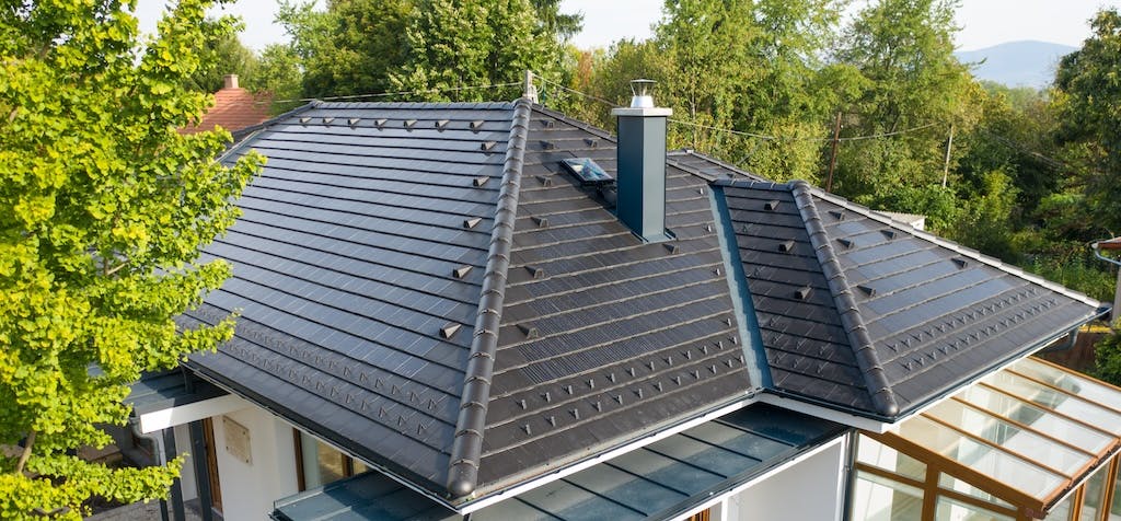 A house with solar roof tiles and a conservatory, green trees in the background