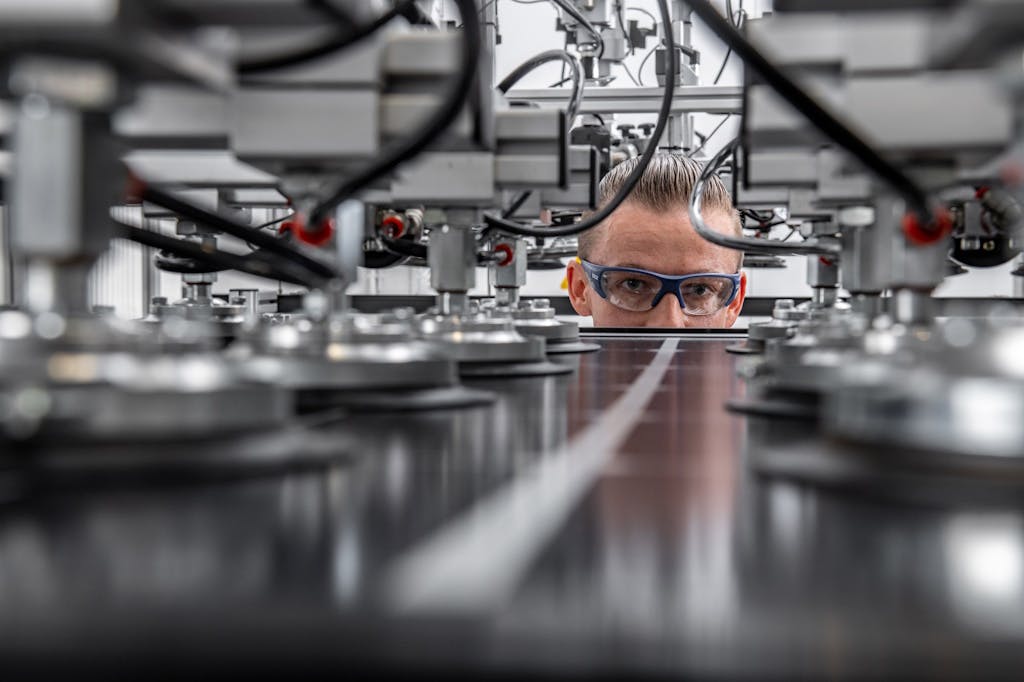 Meyer Burger employee in goggles closely examines a black solar panel as machines apply a finish