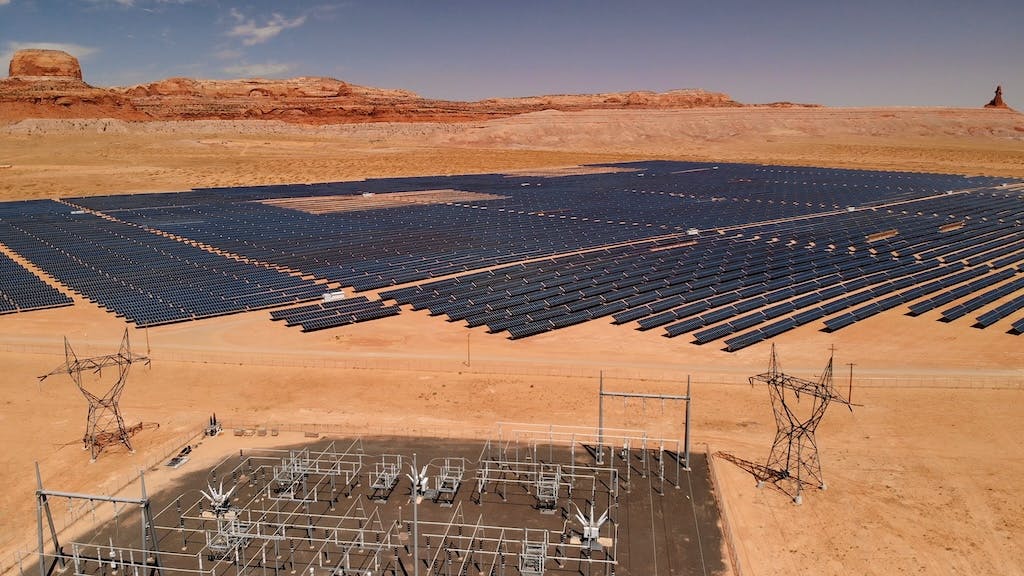 Solar farm in desert, red mountains in background