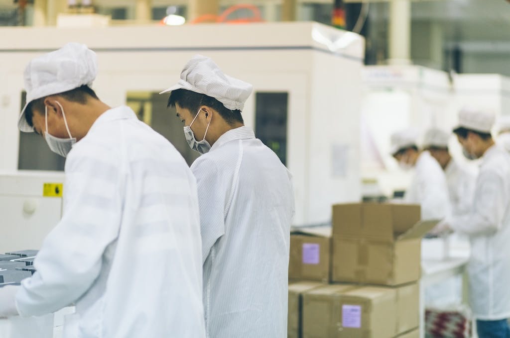 Workers in a solar panel factory along a production line, some cardboard boxes next to them