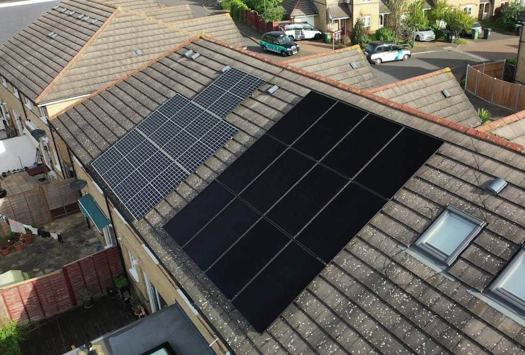 Blue and black solar panels on a brown tiled roof over a terraced and semi-detached house, respectively.