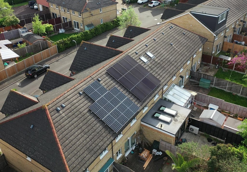 A bird's-eye view of blue and black solar panels on a brown tiled roof over a terraced and semi-detached house, respectively