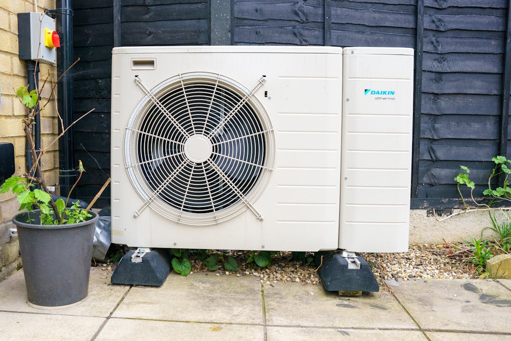 A white and grey heat pump outside on a patio, by a beige wall and dark fence