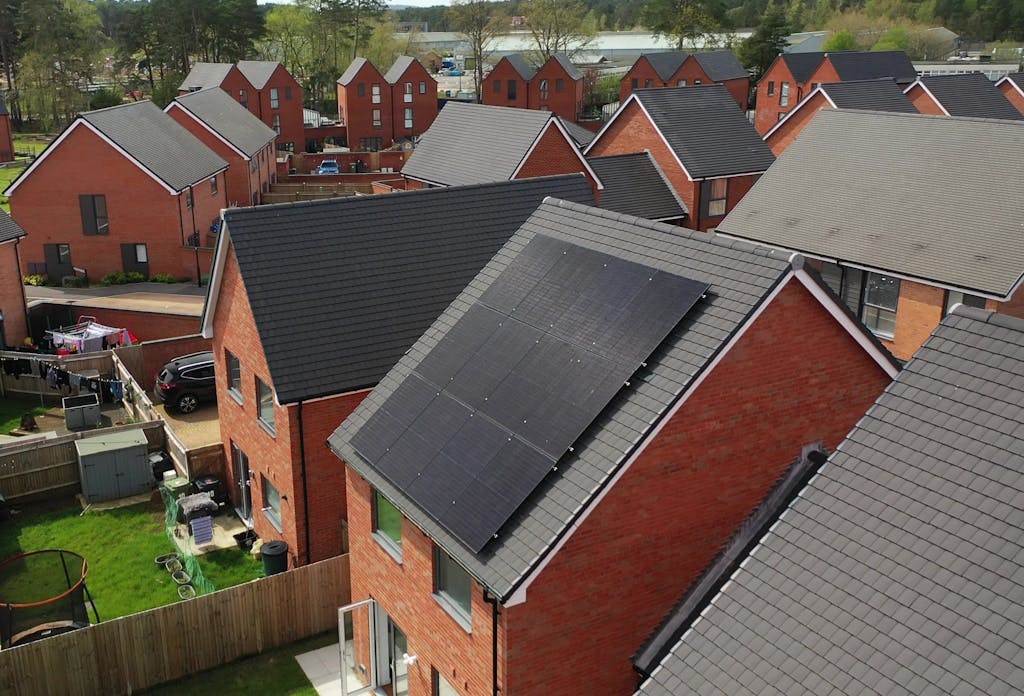 Black solar panels on a grey roof, on a terracotta brick house, next to similar homes