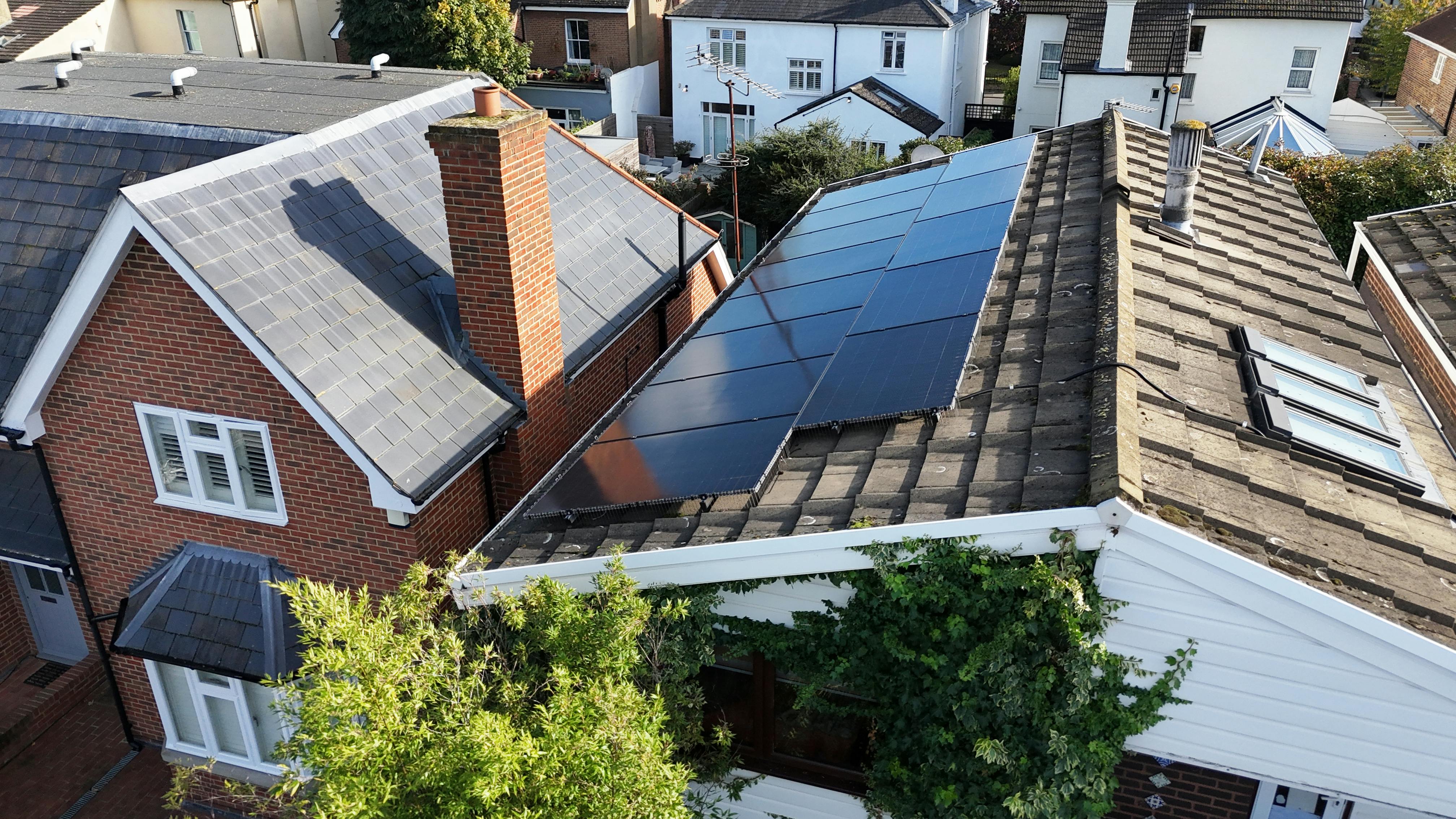 a brown roof with black solar panels on top, next to a brick-coloured house with a grey roof