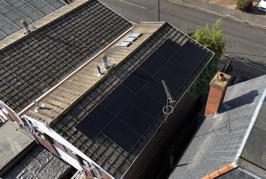 a bird's eye view of a brown roof with black solar panels on top, next to a grey roof