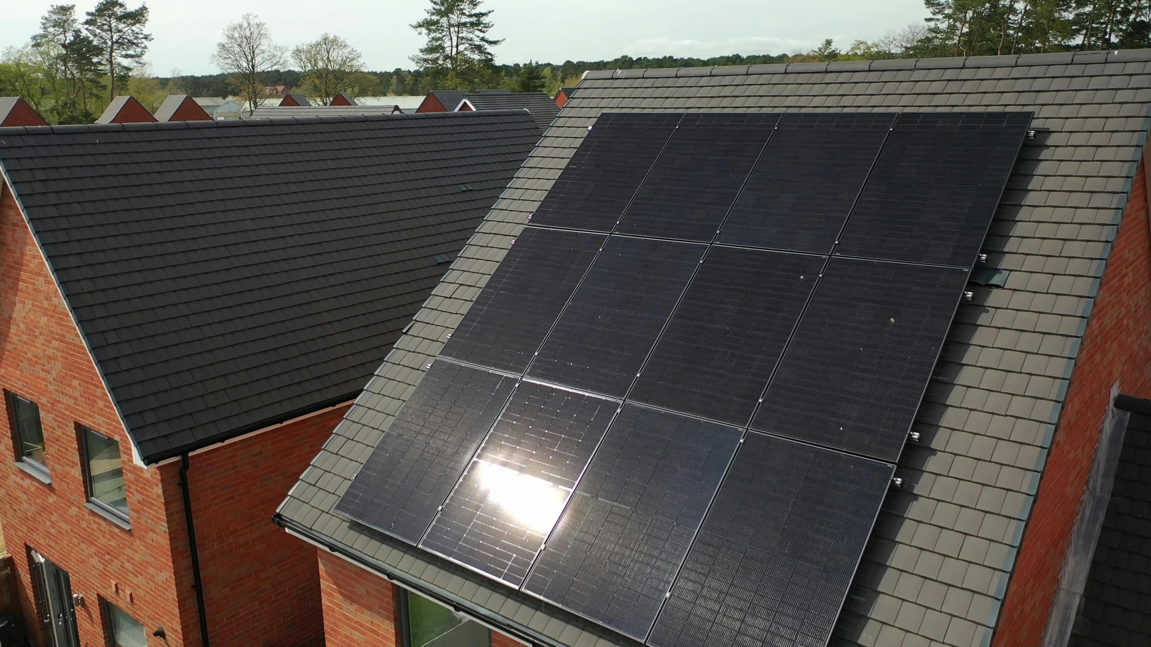 12 black solar panels on the roof of a red-brick new-build house in the UK, sunlight reflecting off them