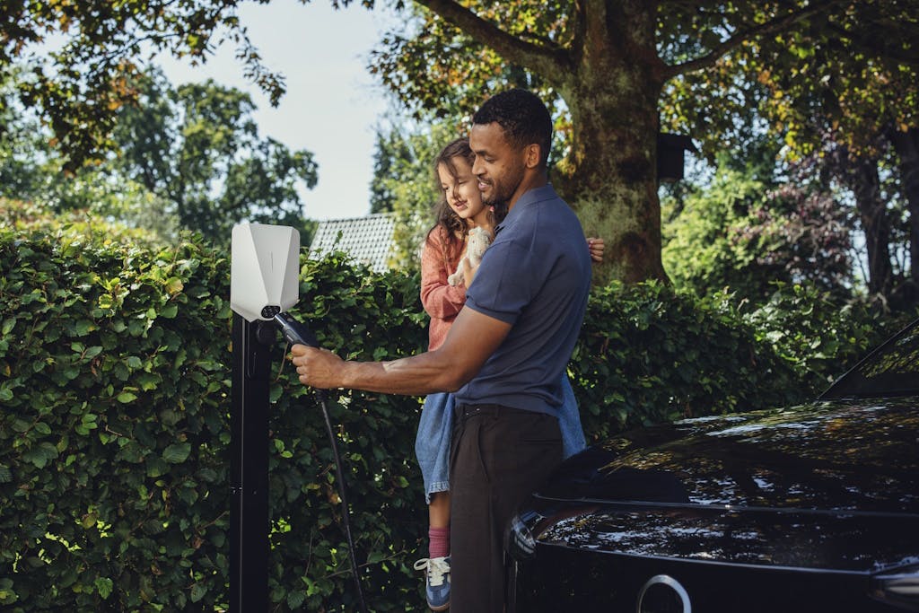 a man holding a child plugs in their electric car charger to an Easee One charging point