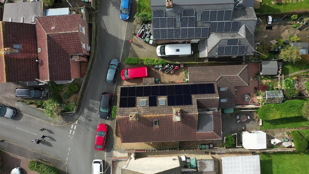 Black solar panel array on a rooftop next to another home with grey solar panels, bird's eye view